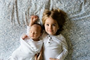 Child lying down next to baby on bedsheets