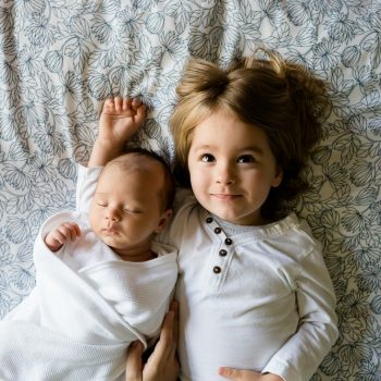 Child lying down next to baby on bedsheets