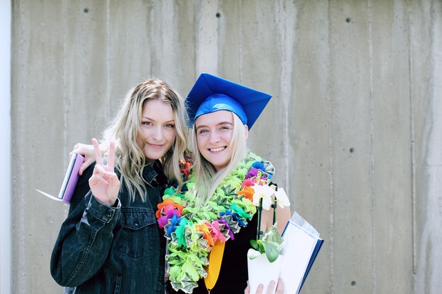 blond adult woman standing with blond high school graduate woman wearing leis