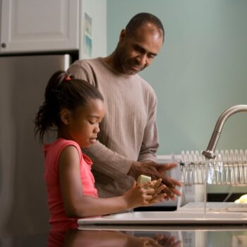 girl washing hands in kitchen with dad