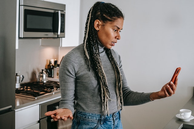 woman making annoyed gesture looking at phone in kitchen