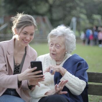 elderly woman and caregiver on park bench looking at phone