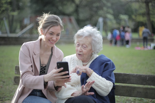 elderly woman and caregiver on park bench looking at phone