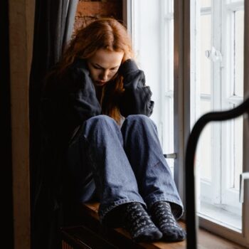 upset teen girl with red hair at window