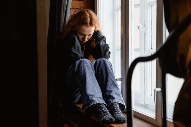 upset teen girl with red hair at window