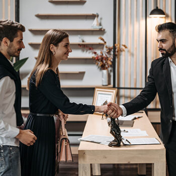 woman standing next to man shaking hands with man across the table