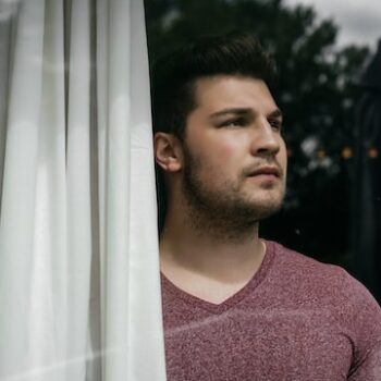 man looking out window uneasy